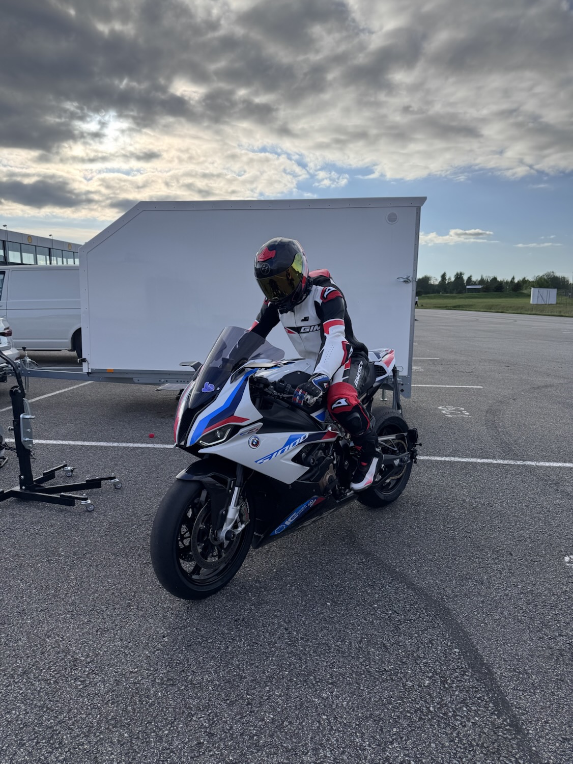 Rider seated on the S 1000 RR in the paddock with the white trailer behind
