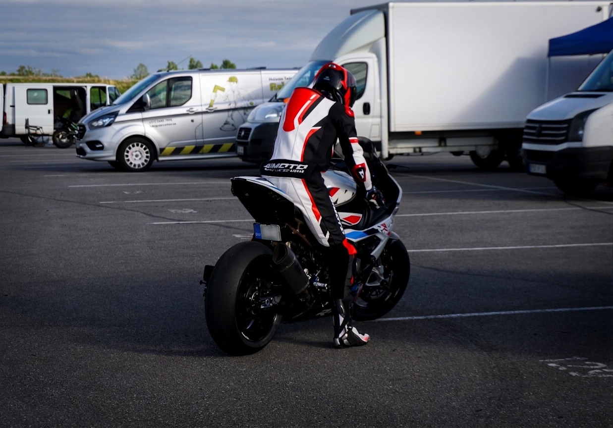 Rider in white and red leathers walking a white S 1000 RR through the paddock at Porsche Ring