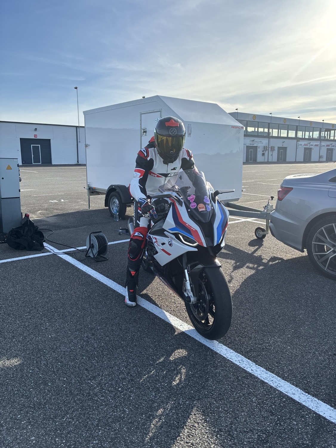 Rider in full leathers sitting on the bike in front of the trailer, morning sun