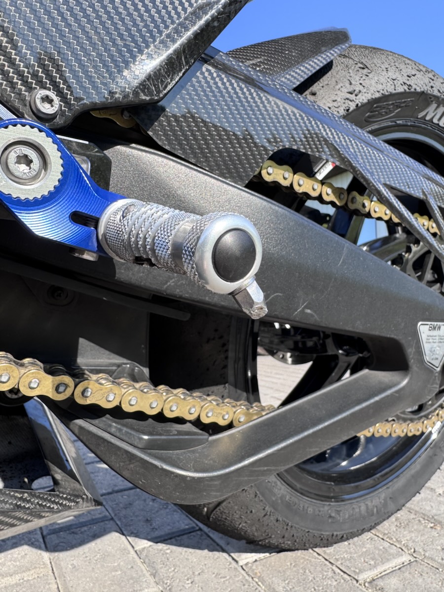 Close-up of a billet rearset footpeg next to the gold chain
