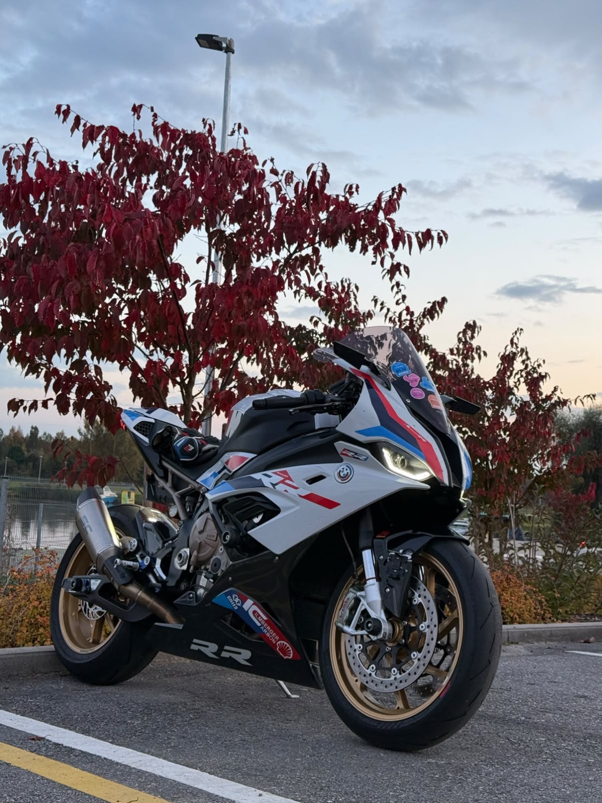 The bike parked under a red autumn tree at dusk with track stickers on the screen