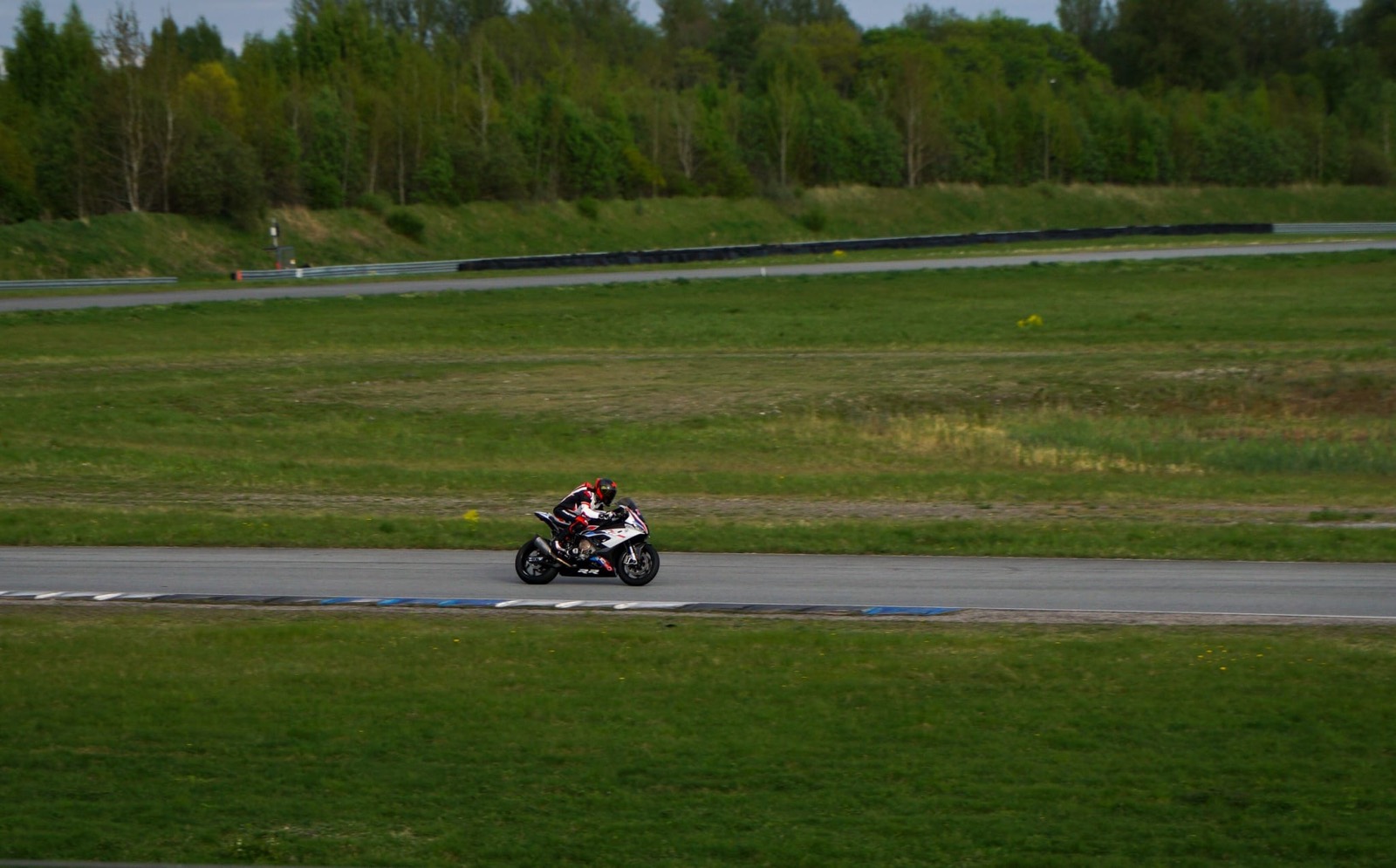 Wide shot of the bike on the back straight with trees behind