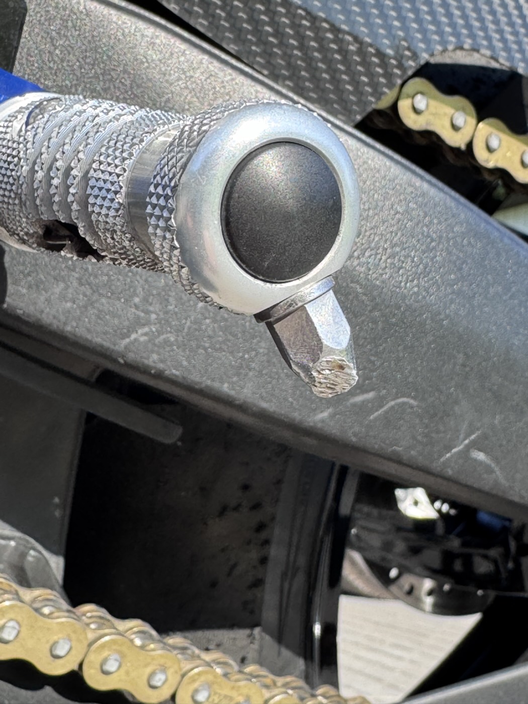 Macro shot of a knurled aluminium footpeg with a worn hero blob