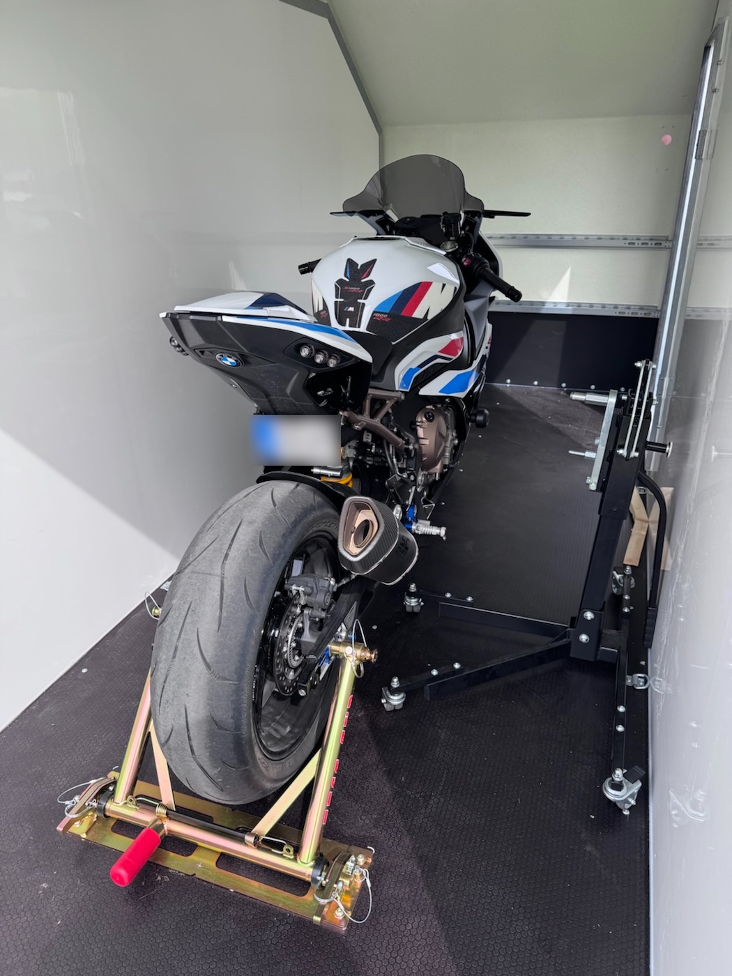 The bike from behind in the trailer, rear wheel clamped in a gold chock